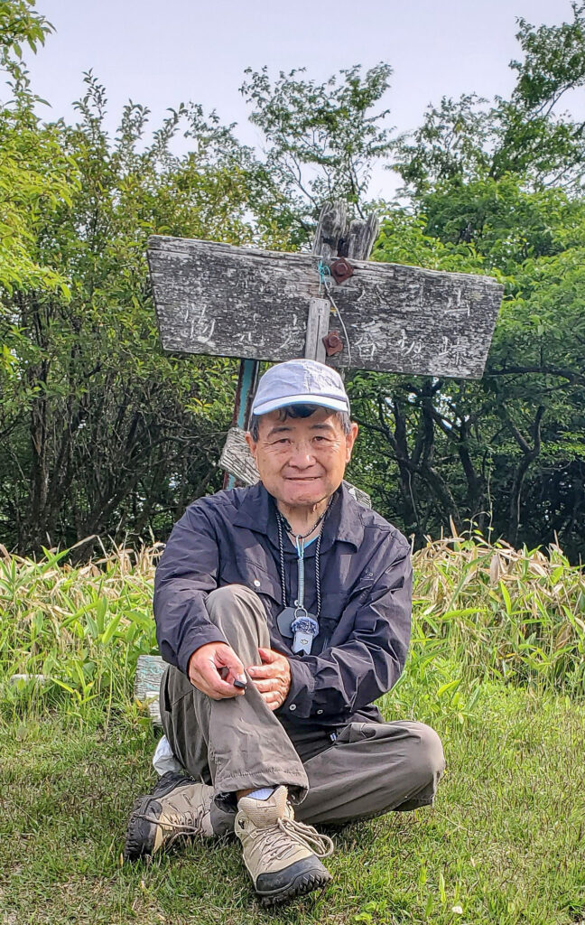物見山の山頂標識前で腰を下ろすShin