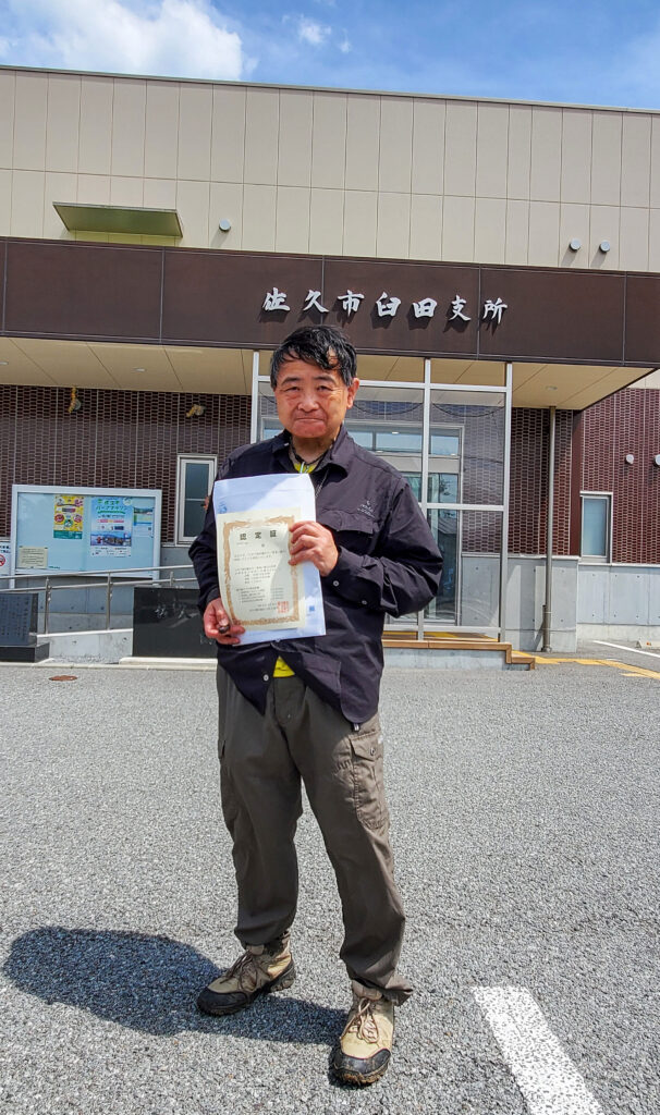 佐久市臼田支所前で「日本で海岸線から一番遠い地点」の認定証を手にするShin