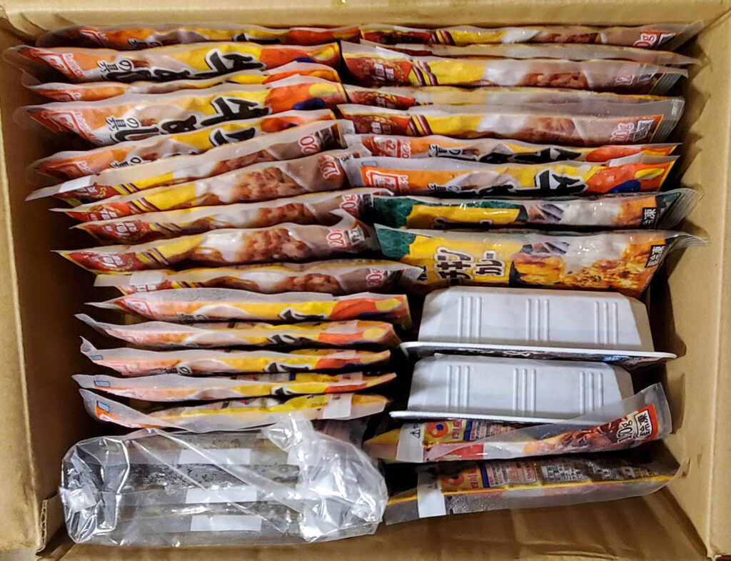 松屋の「訳あり30食セット」を開封した様子。段ボール箱の中に牛めしの具やカレー、牛ホルモン焼きなどの冷凍食品がぎっしり詰められている。