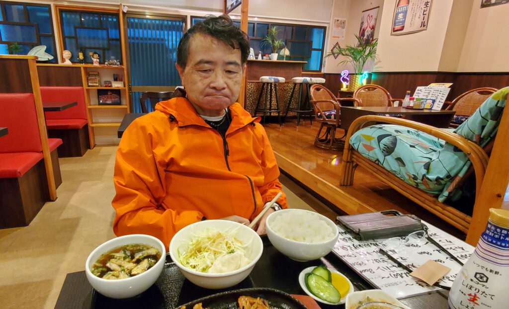 栃木県小山市のごはんや天神で、スタミナ焼肉定食を前に席に着くShin。