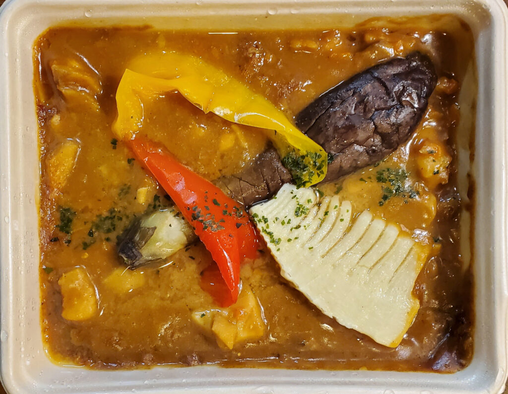 DELIPICKSの魚介のラグーカレー。茶色いカレーソースの中に、魚介、ナス、赤と黄色のパプリカ、たけのこが入っている。