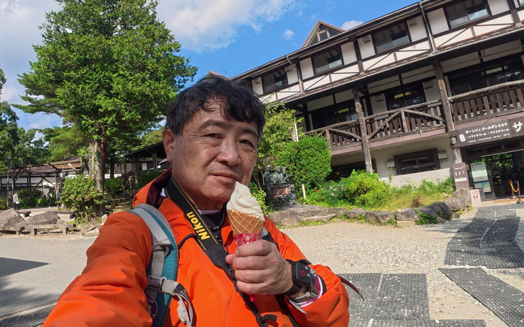 那須高原の南ヶ丘牧場でソフトクリームを手にするShin。背景には牧場の建物が見える。