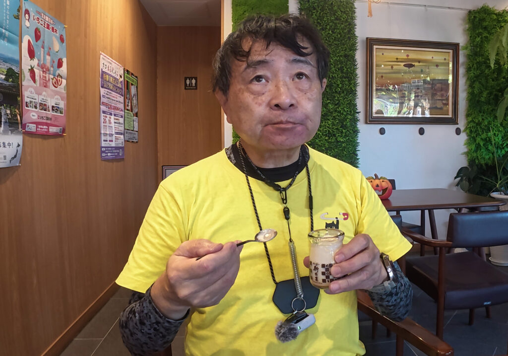 新井屋のカフェスペースで黄色いTシャツ姿のShinが味噌ぷりんをスプーンで食べている様子